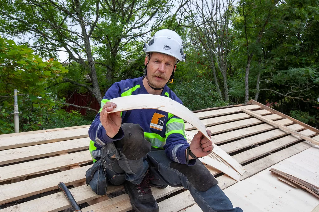 Lauri Leppänen taivuttaa pärettä nähdäkseen, miten päin se kuuluu naulata. Syiden suunnalla on väliä, jotta vesi pääsee valumaan katolta.